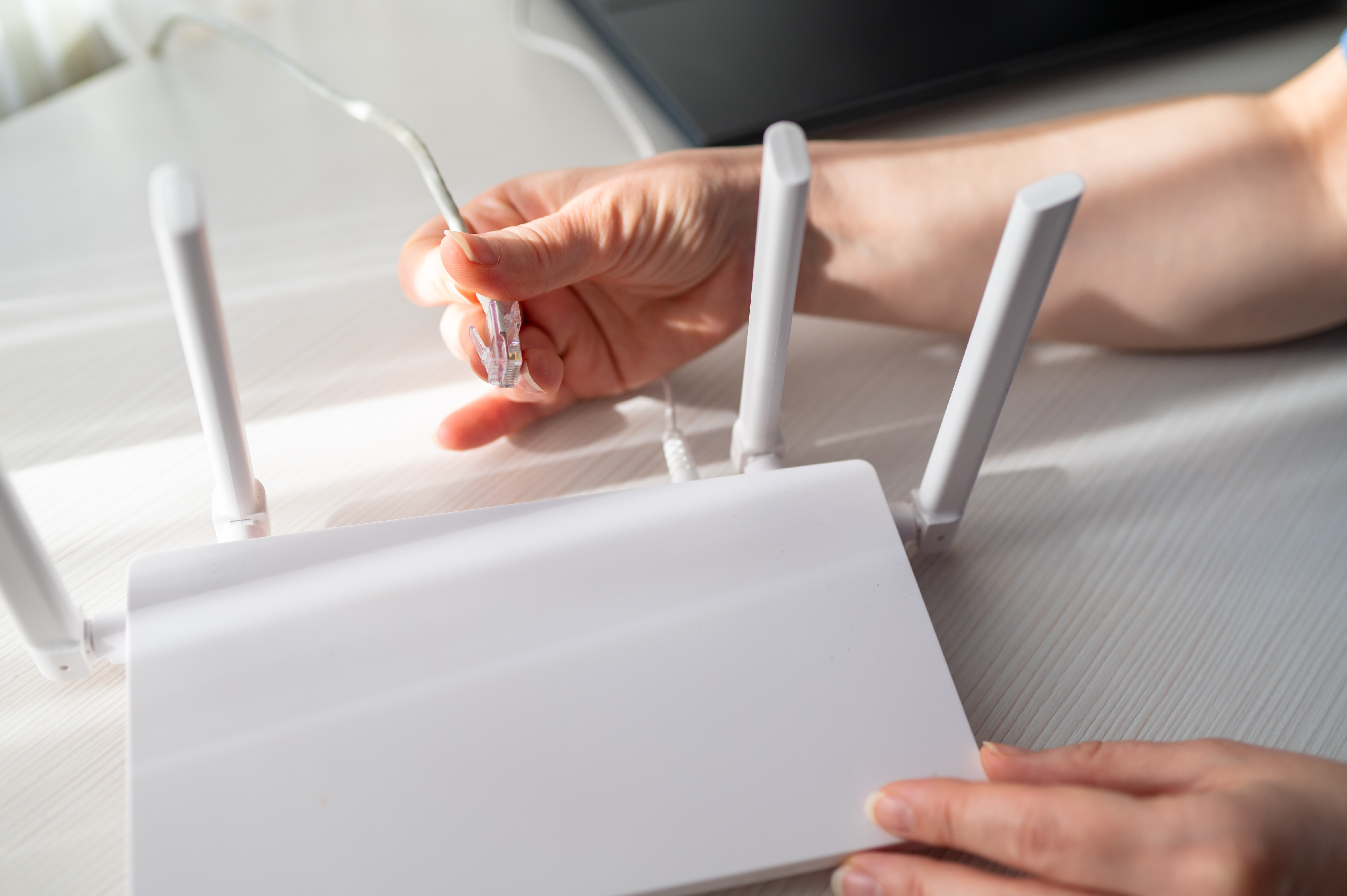 Close up of a person plugging a network cable into a wireless router with four antennas. Image represents internet setup, technical support, hardware connection and high speed data transfer