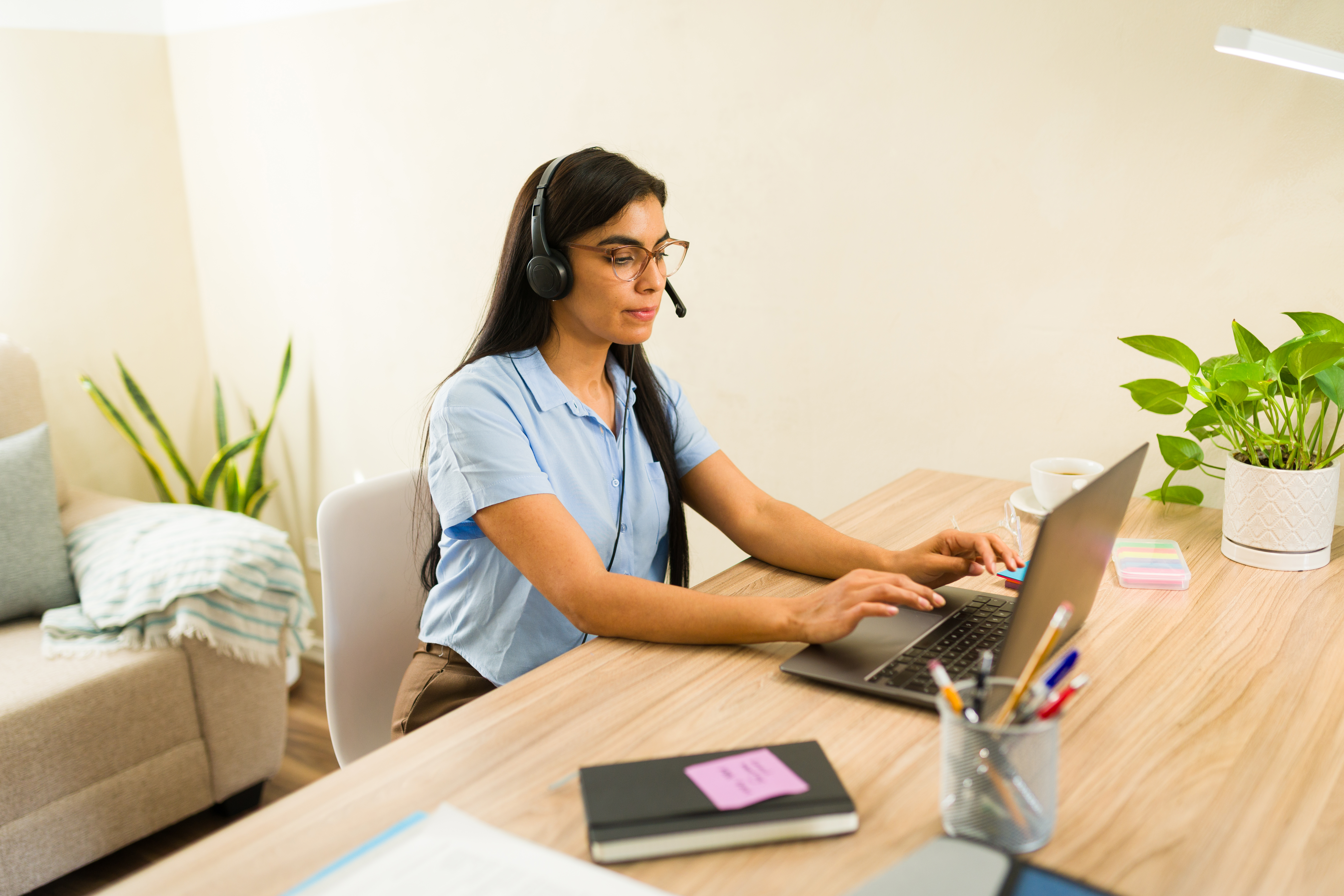 Professional businesswoman working from a home office, talking on a video call with a headset and typing on a laptop